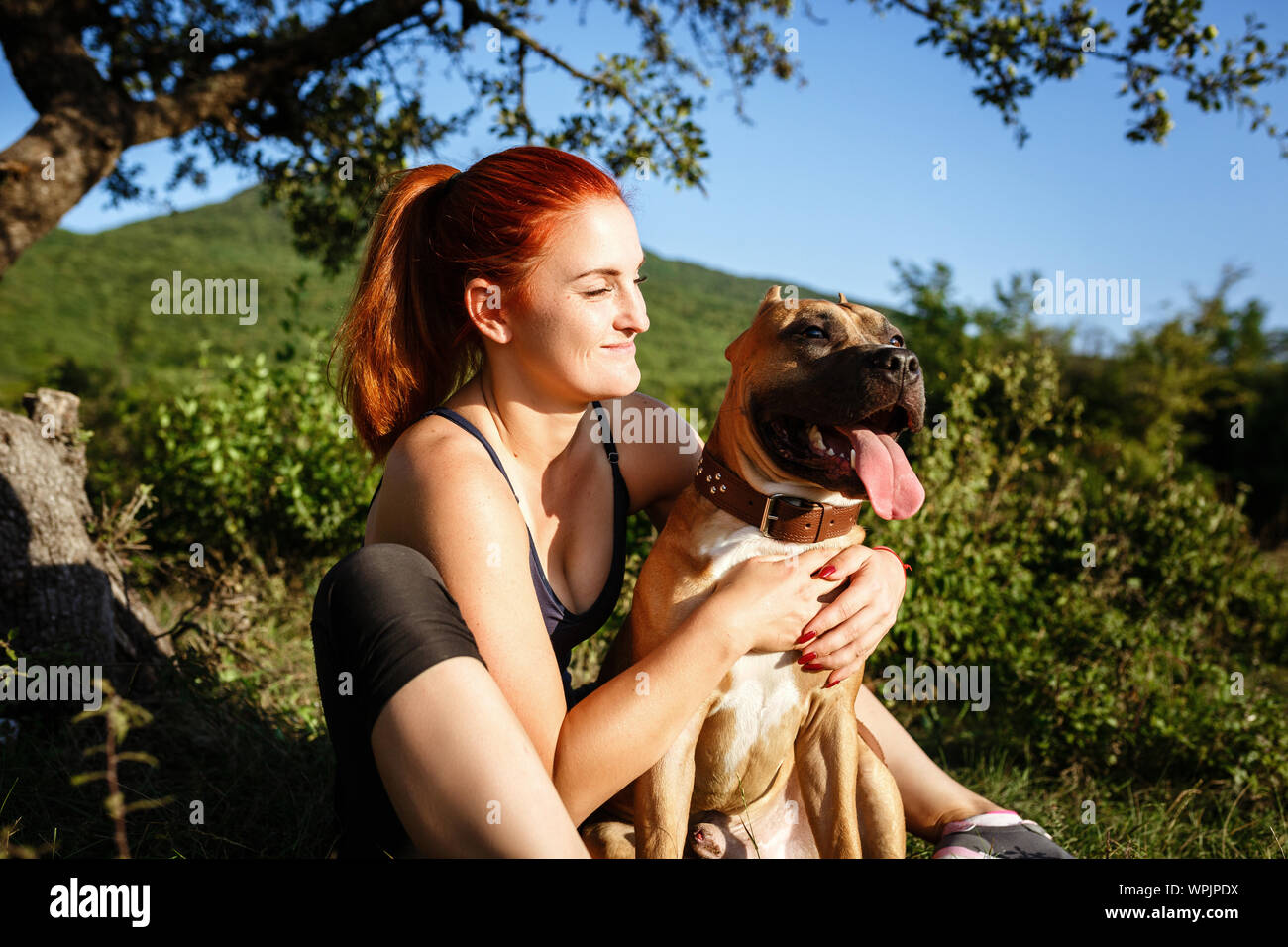 jouful young girl caressing their dog, wearing sport clothing, enjoying their time and vacation in sunny park Stock Photo