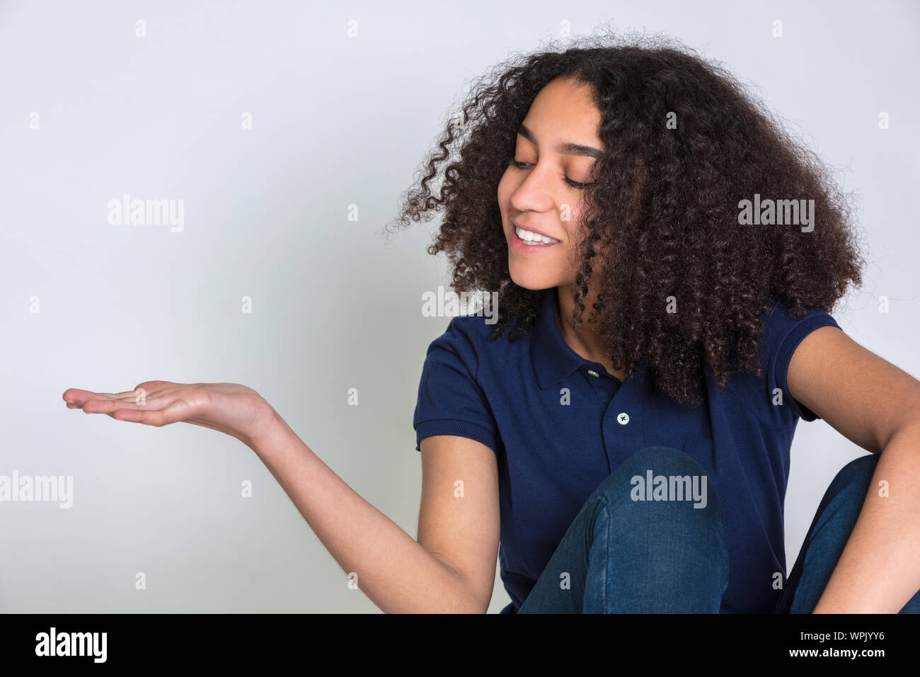 Studio shot of a biracial mixed race African American girl female teen teenager young woman with curly hair,  looking at her empty hand outstretched r Stock Photo