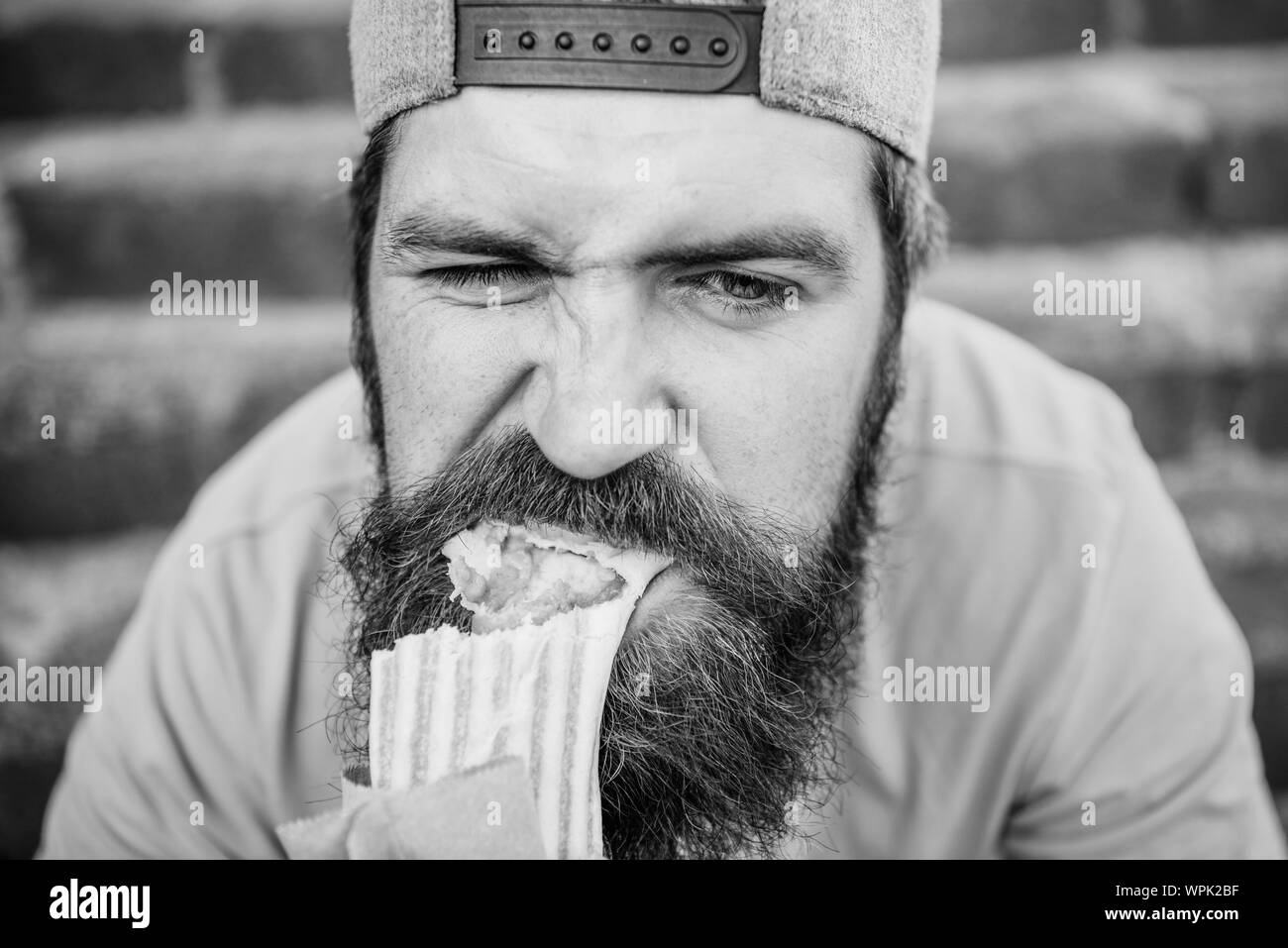 Junk food. Snack for good mood. Unleashed appetite. Street food concept. Man bearded eat tasty sausage. Urban lifestyle nutrition. Carefree hipster eat junk food while sit stairs. Guy eating hot dog. Stock Photo