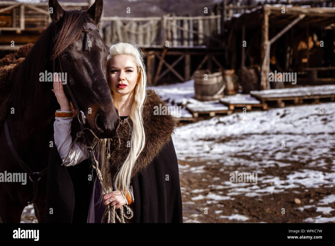 Outdoors portrait of beautiful furious scandinavian warrior ginger woman in a traditional clothes with fur collar, with sword in her hand and wooden V Stock Photo