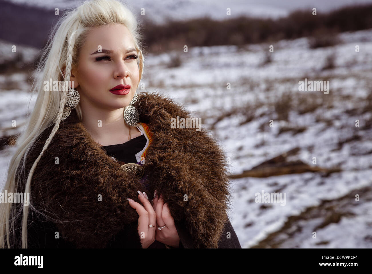 Outdoors portrait of beautiful furious scandinavian warrior ginger woman in a traditional clothes with fur collar, with sword in her hand and wooden V Stock Photo