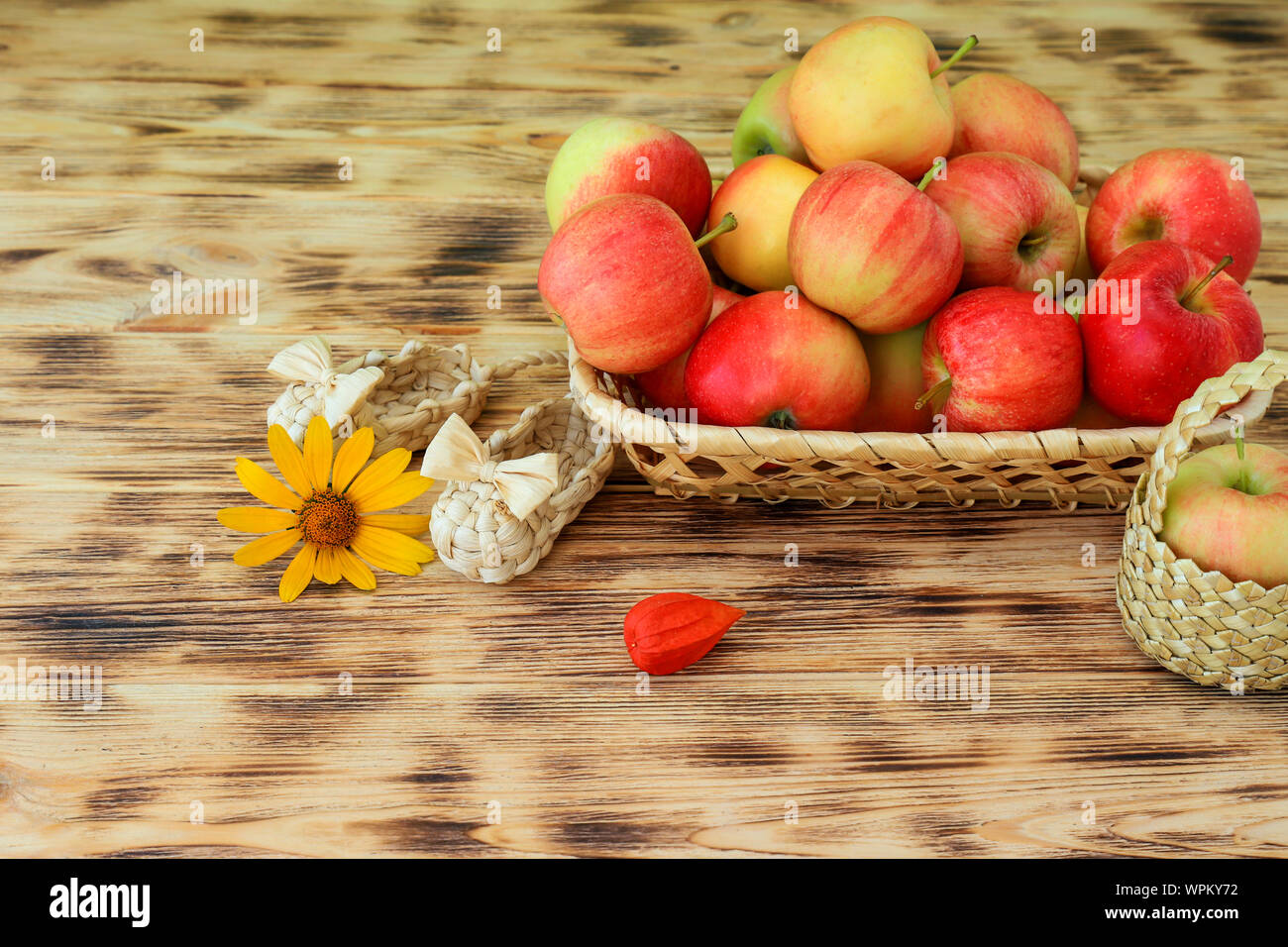 Red apples and autumn flowers lie in a wicker plate on a wooden table. Wicker bast shoes and apples in a basket. Healthy food and lifestyle Stock Photo