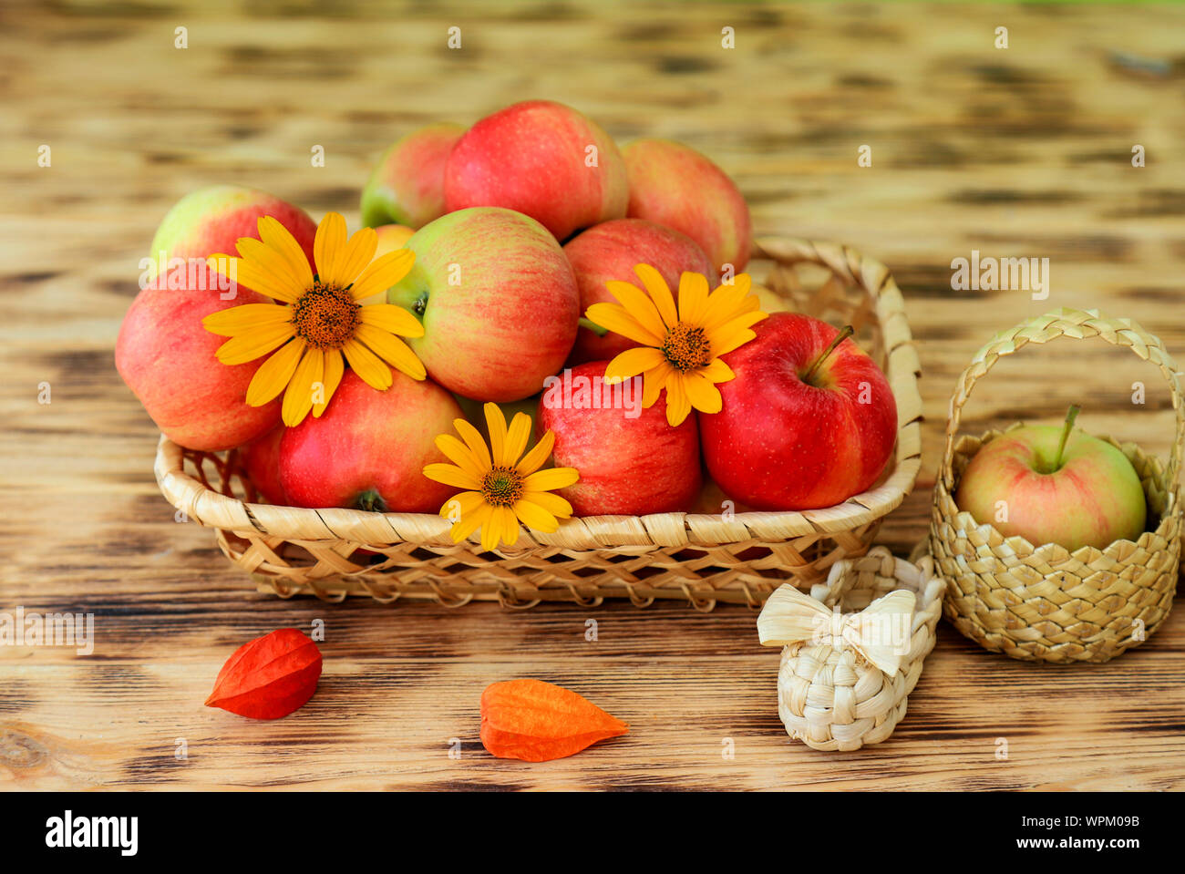 Red ripe apples and autumn flowers lie in a wicker plate on a wooden table. Wicker bast shoes and apples in a basket. Healthy food and lifestyle Stock Photo