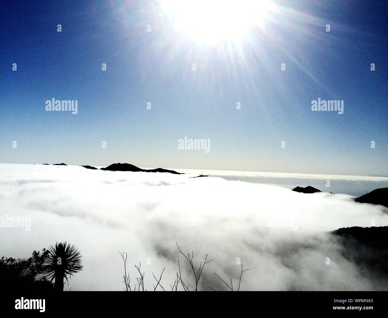Scenic View Of Sun Flaring Above Fog Covering Mountain Stock Photo