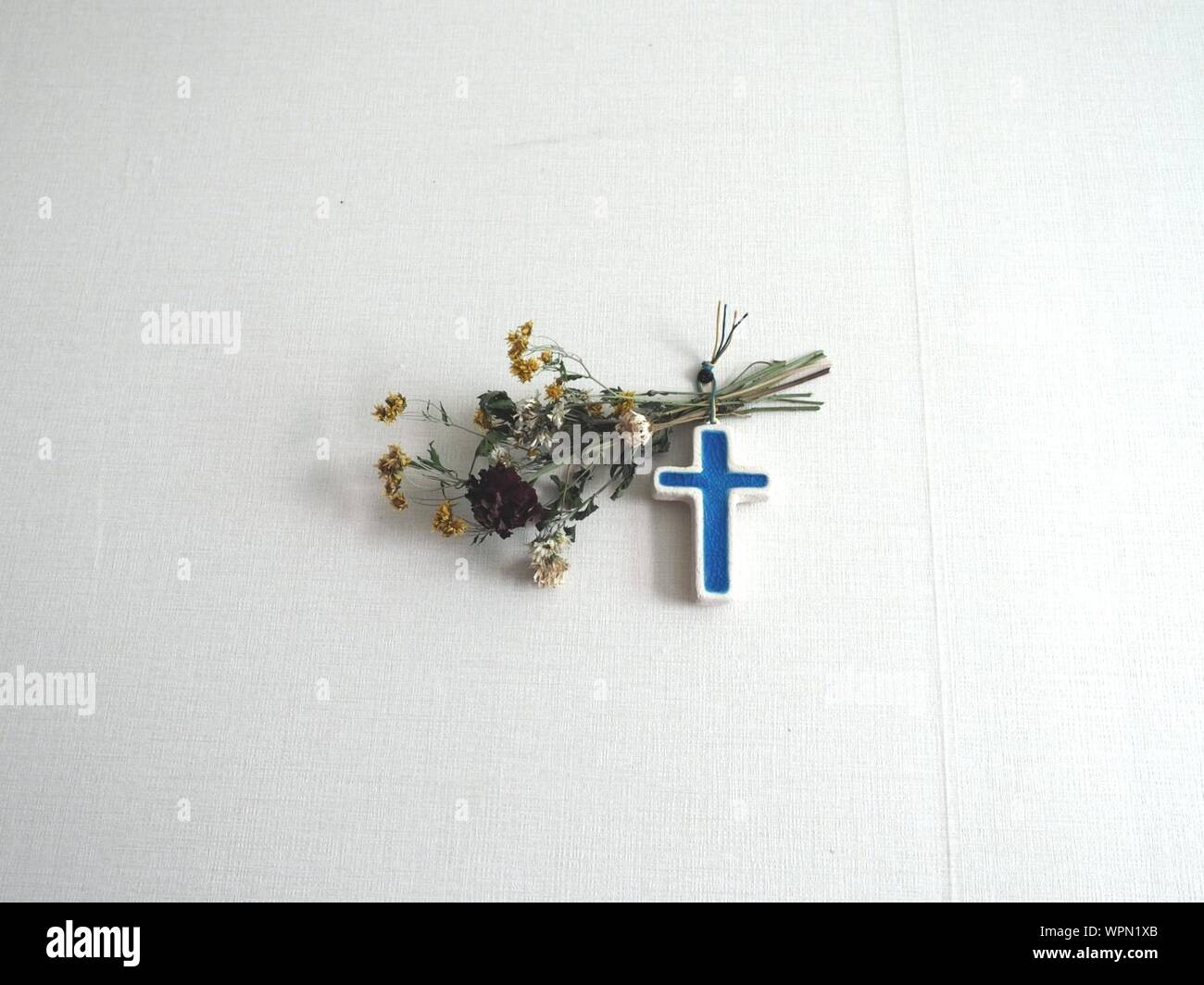 Blue Cross With Flowers Hanging On White Wall Stock Photo