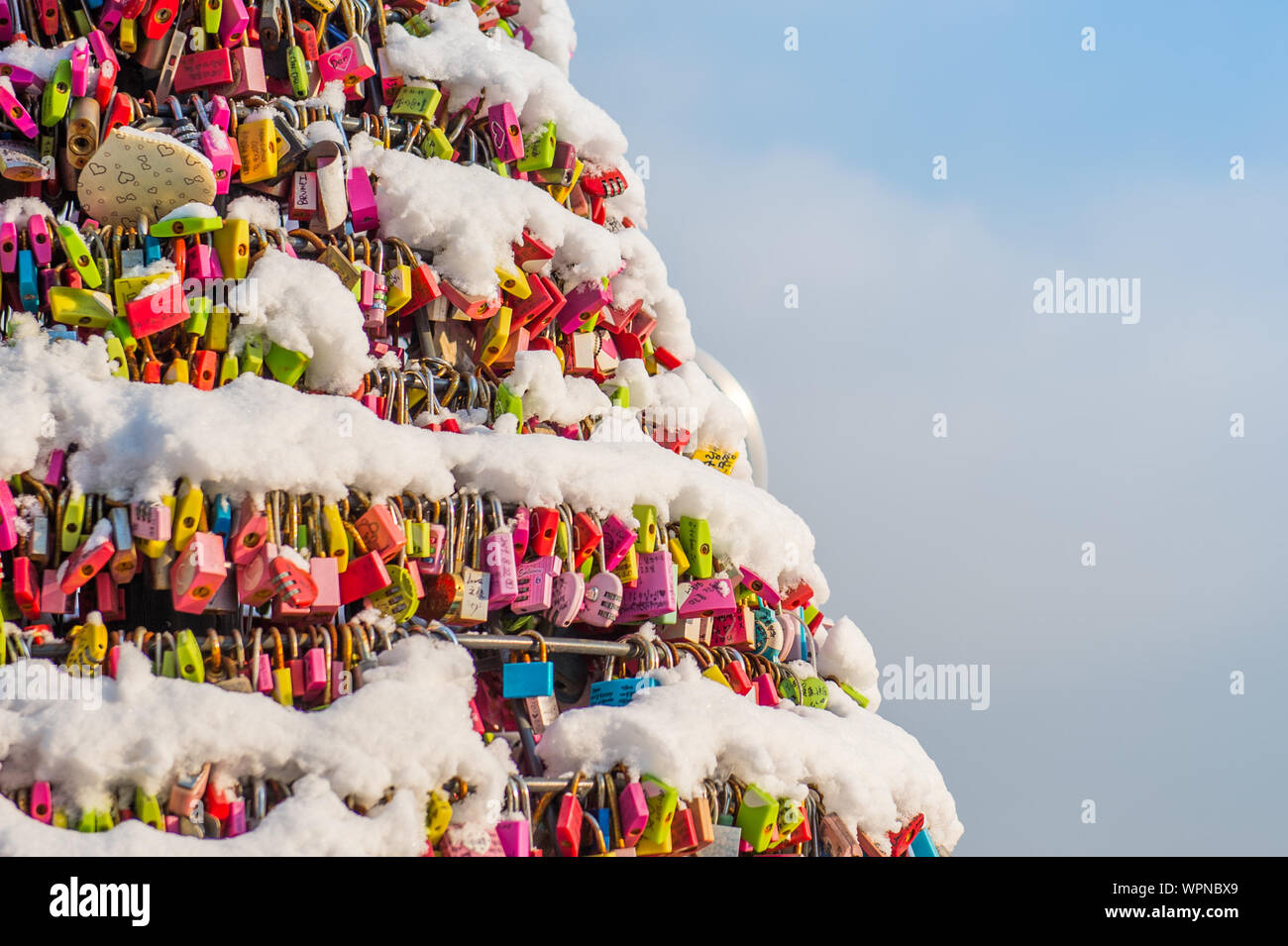 Close-up Of Colorful Padlocks Hanging On Frozen Railings Against Sky Stock Photo