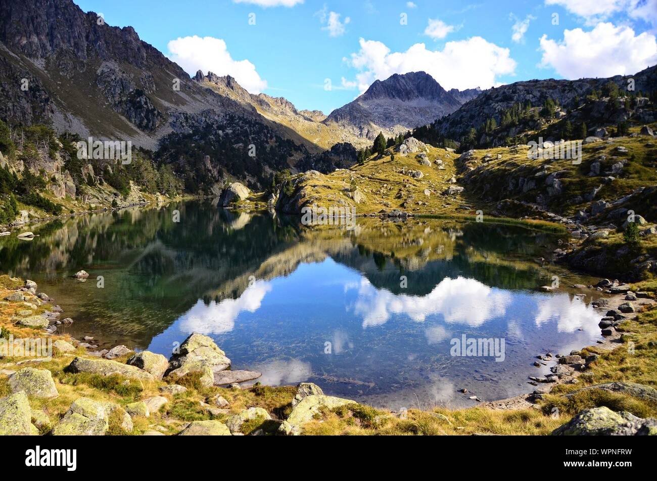 Scenic View Of Lake Nestled In Mountains Against Cloudy Sky Stock Photo
