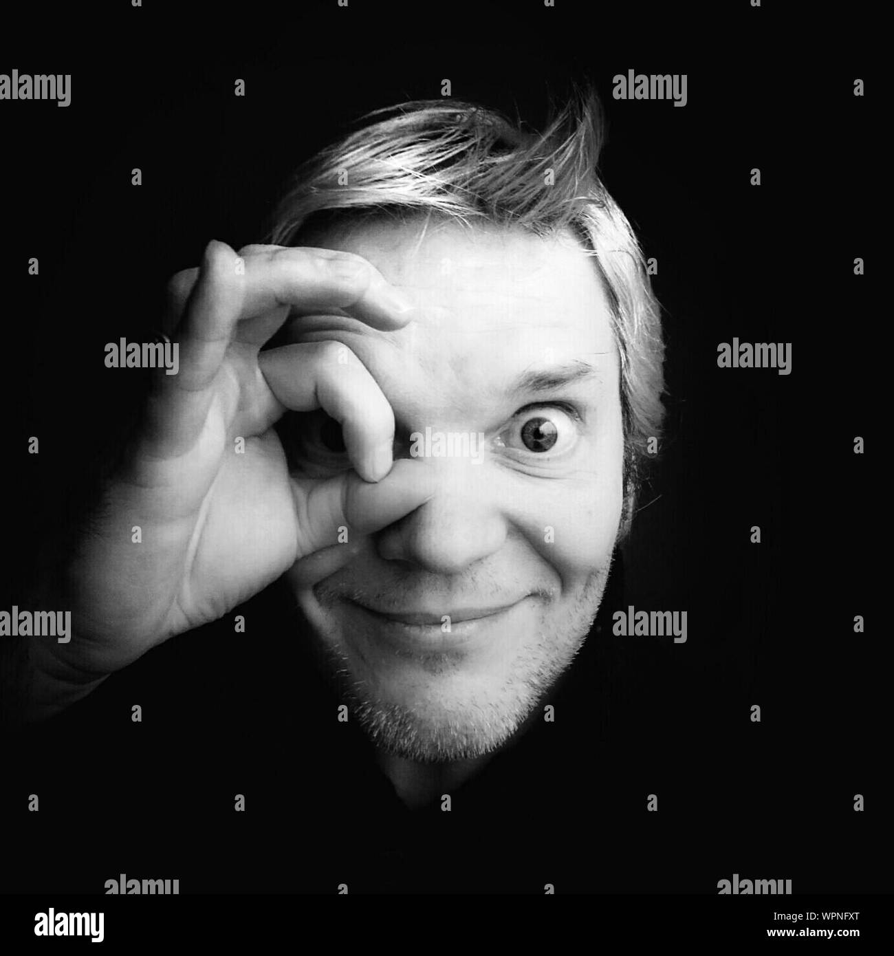 Portrait Of Man Circling Eye With Fingers Against Black Background Stock Photo