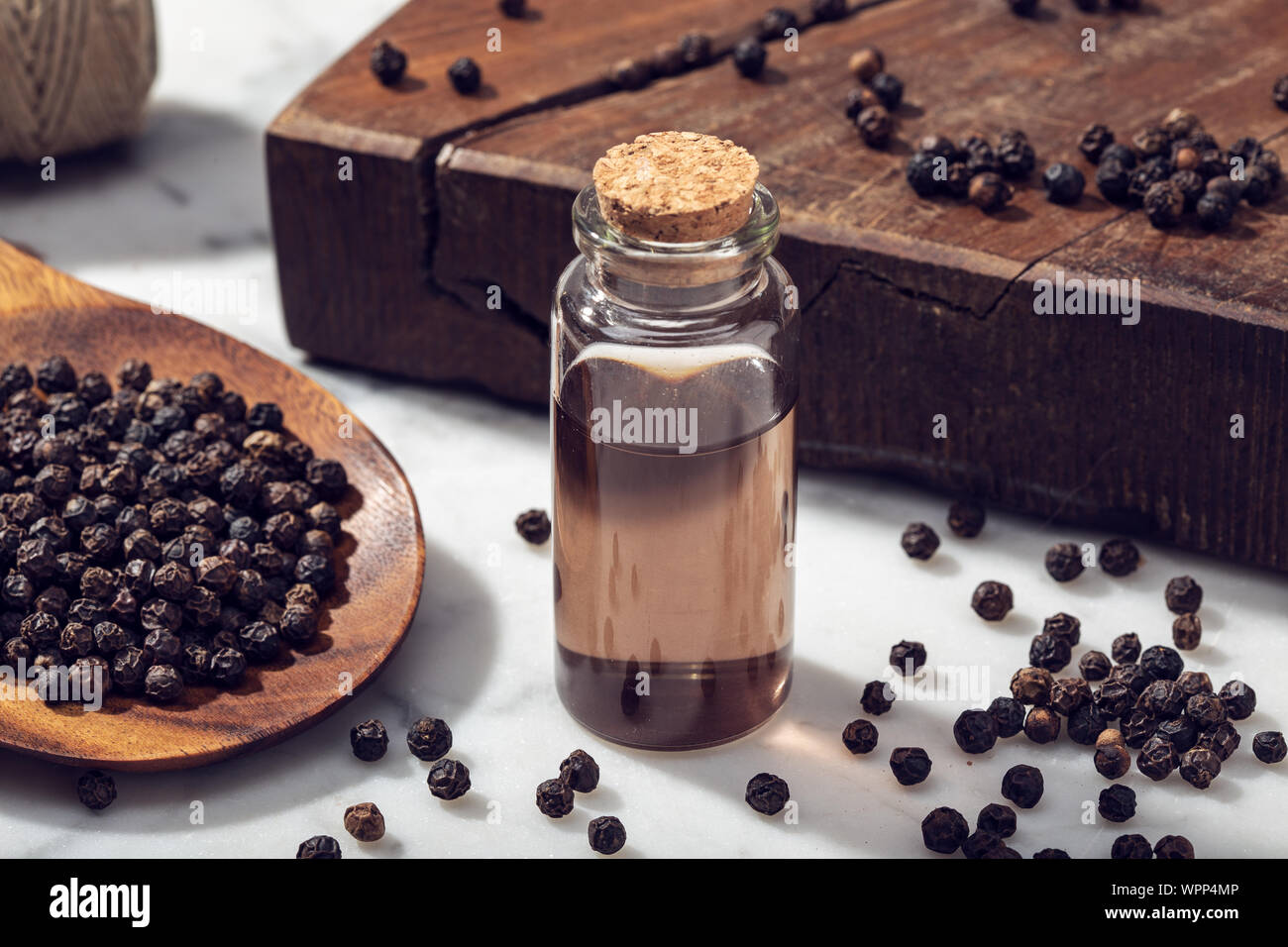 Black pepper essential oil on marble table. Peppercorn oil bottle Stock