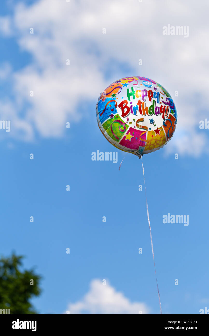 Colorful happy birthday balloon on a blue sky background in summertime ...
