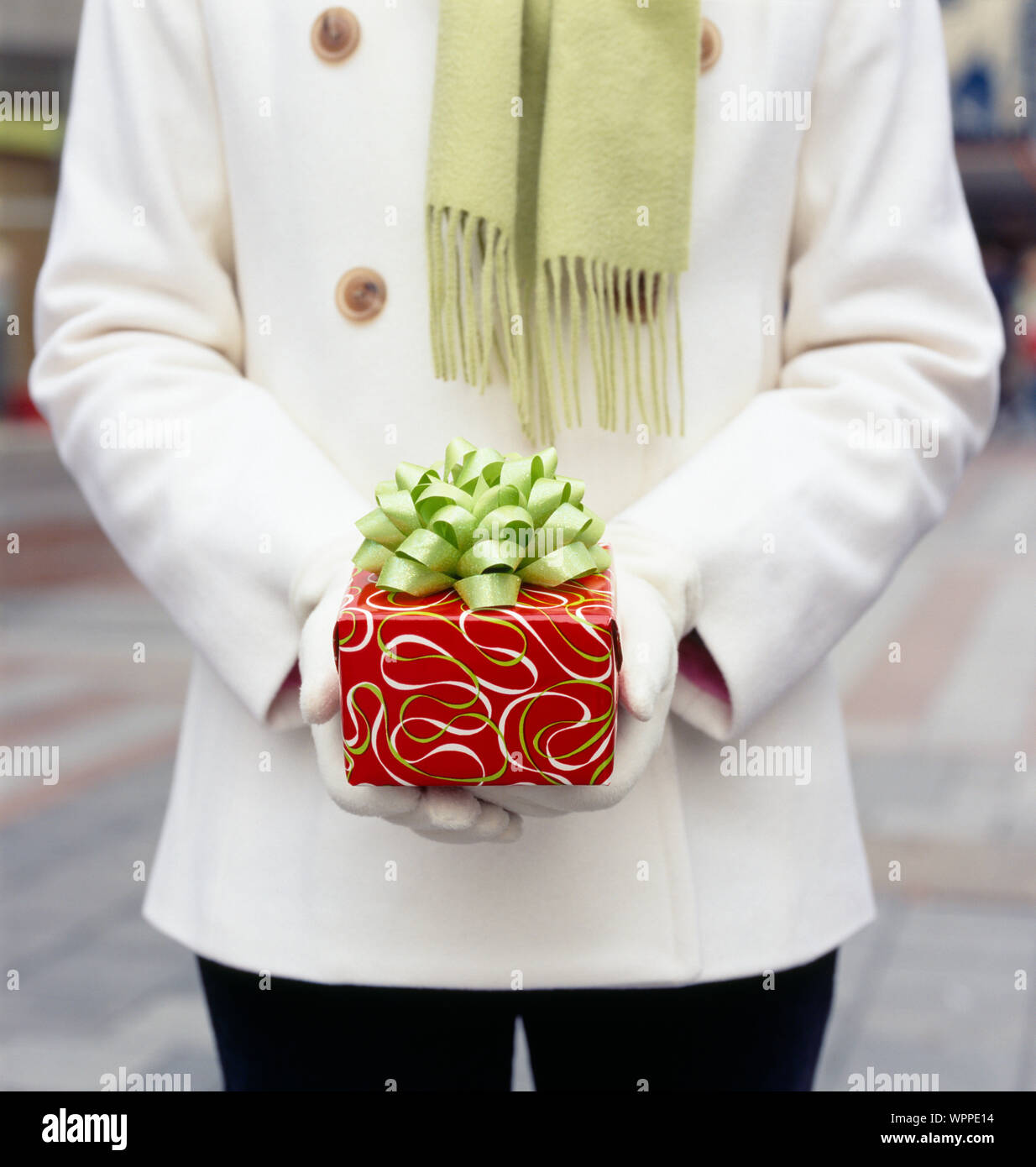 Woman in white wool coat holding Christmas gift present with festive wrapping paper and bow. Holiday gifts presents background. Stock Photo