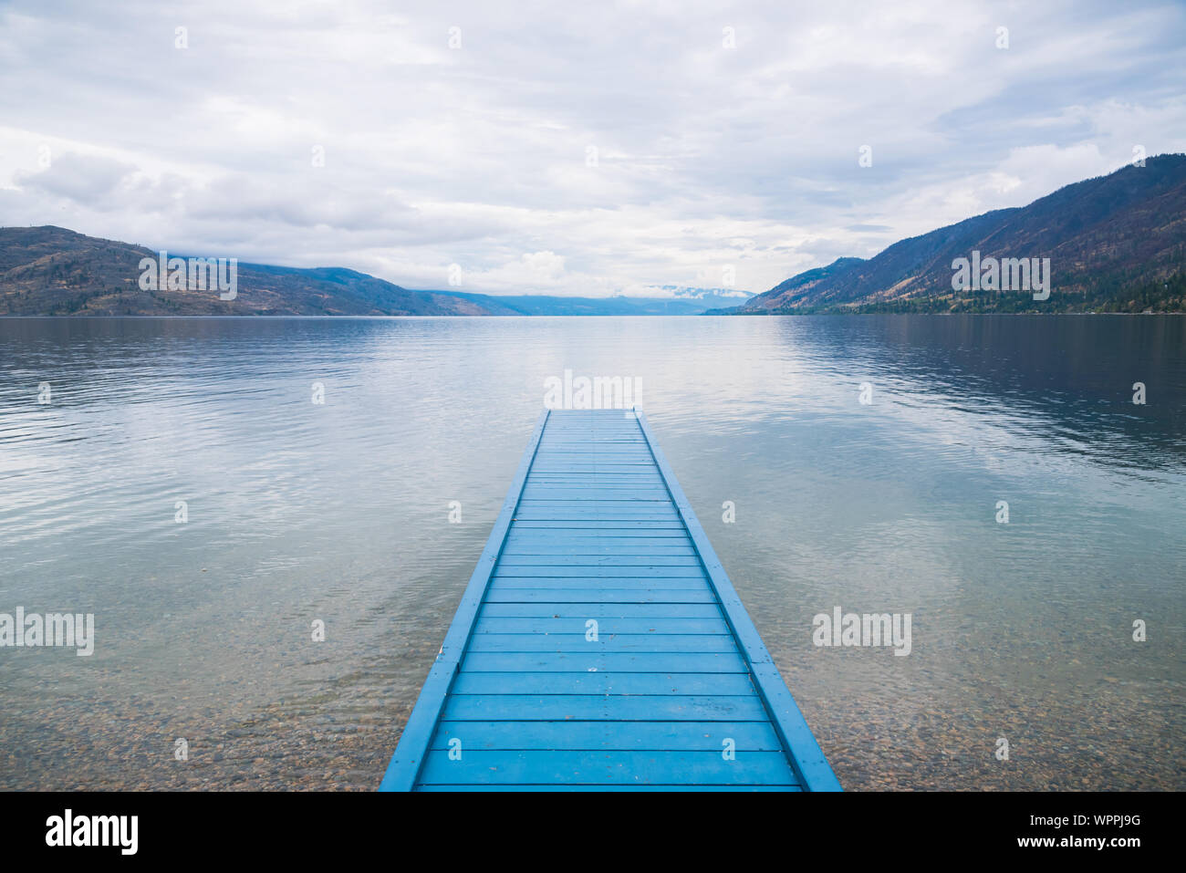 Blue painted dock on lake with view of mountains and cloudy sky Stock Photo
