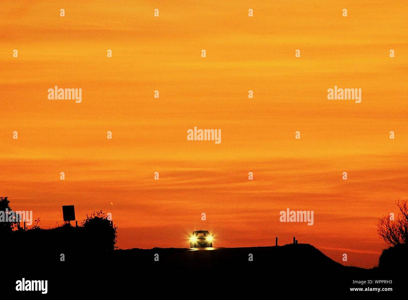 Illuminated Headlights Of Car On Road Against Sunset Sky Stock Photo