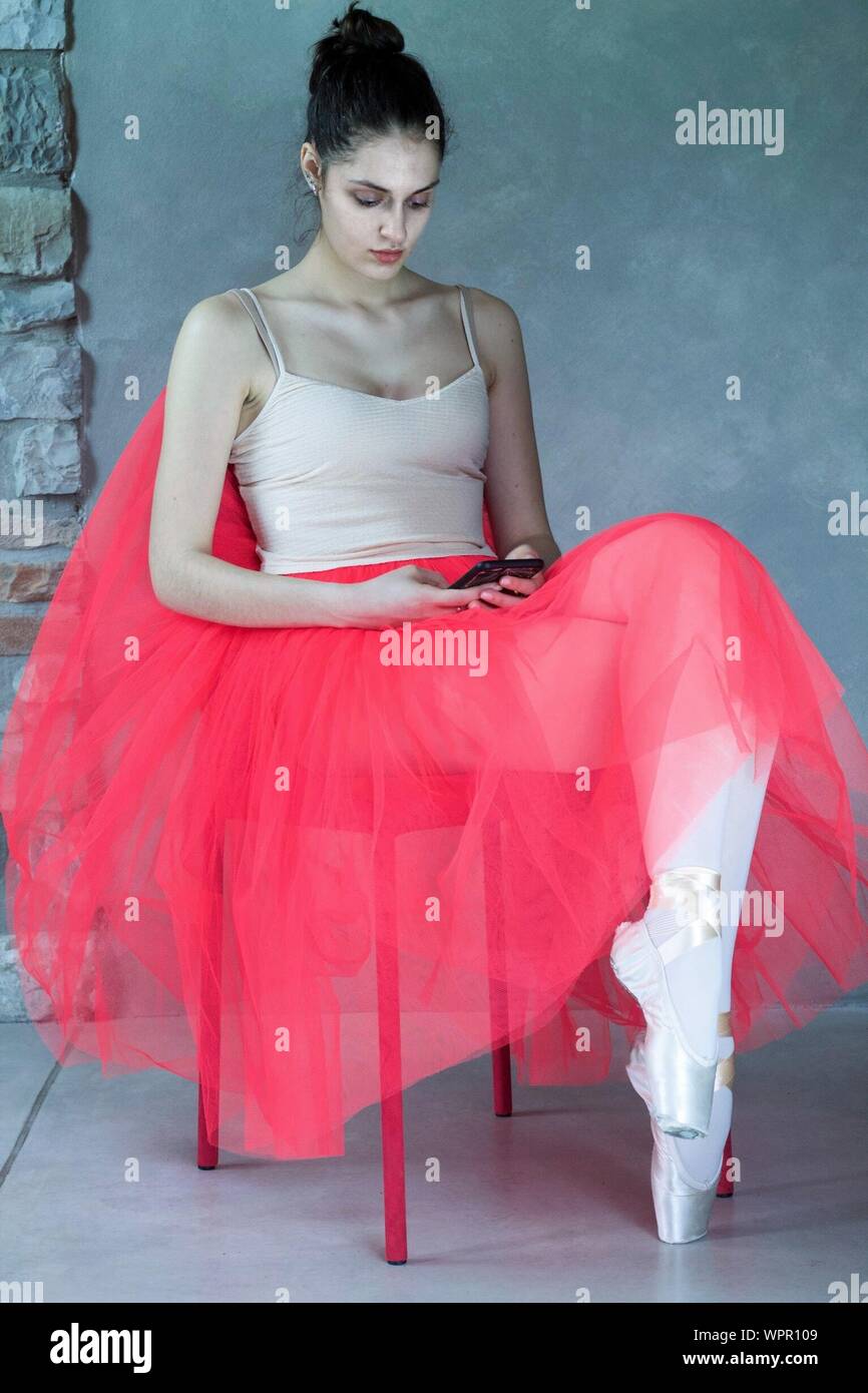 Full Length Of Ballet Dancer Sitting On Chair While Using Phone Stock Photo