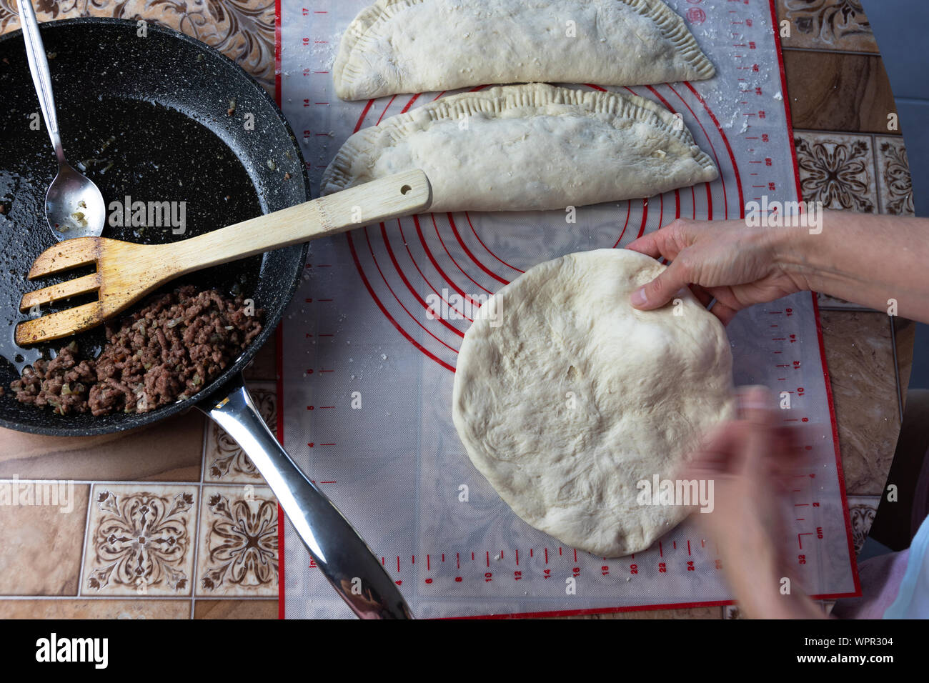 Close up of a woman's hands making dough for homemade bread, empanadas. female baker preparing bread on a silicone baking sheet. frying pan with grinn Stock Photo