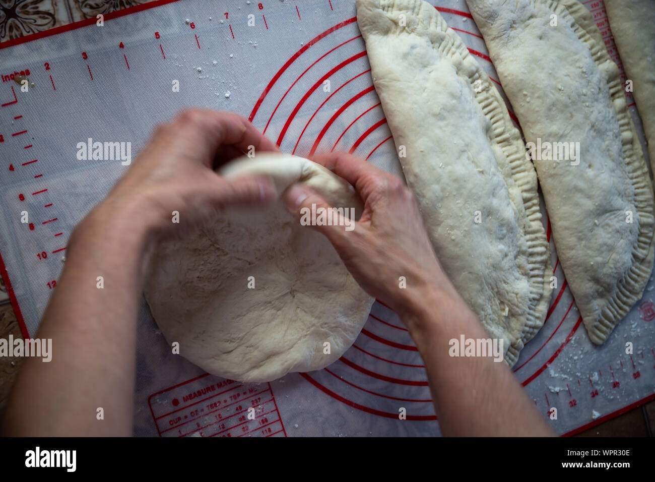 Close up of a woman's hands making dough for homemade bread, empanadas. female baker preparing bread on a silicone baking sheet Stock Photo