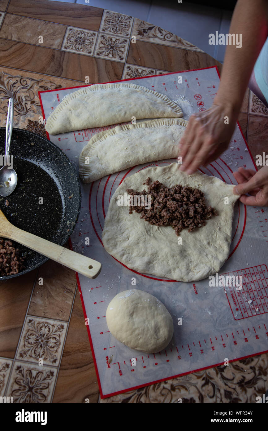 Close up of a woman's hands making dough for homemade bread, empanadas. female baker preparing bread on a silicone baking sheet. frying pan with grinn Stock Photo