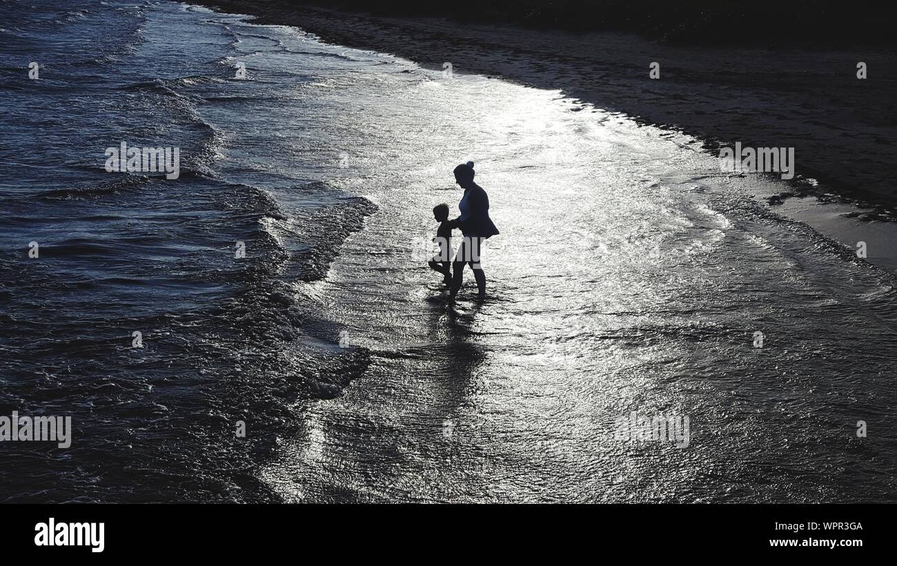 High Angle View Of Silhouette Mother And Son Walking In Sea During