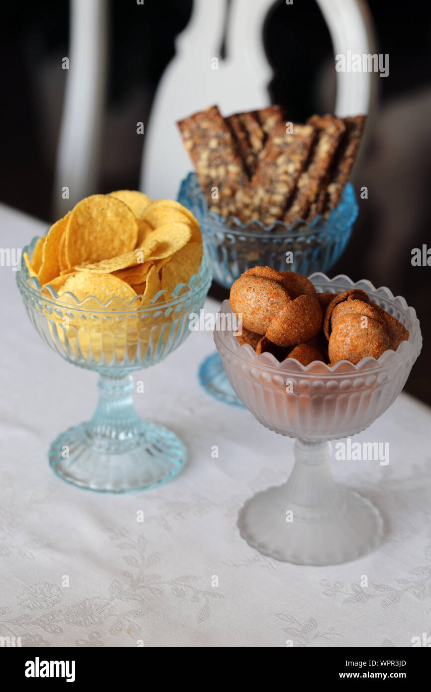 Chips and dry bread bites in beautiful glass bowls. Crunchy and delicious snacks served in a Finnish home. Closeup still life photo, a soft background. Stock Photo