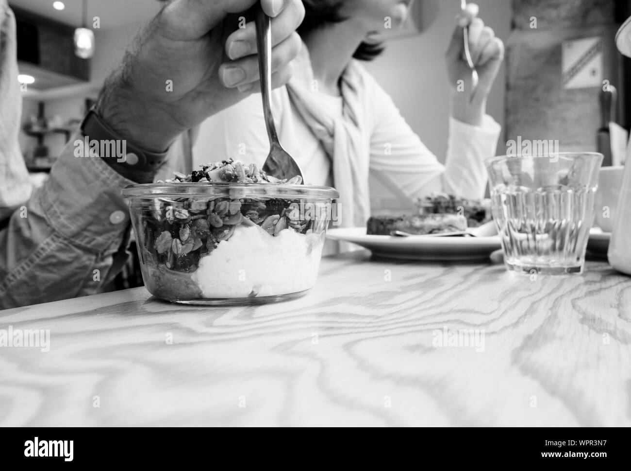 Side view of man and woman eating delicious yogurt with muesli drinking