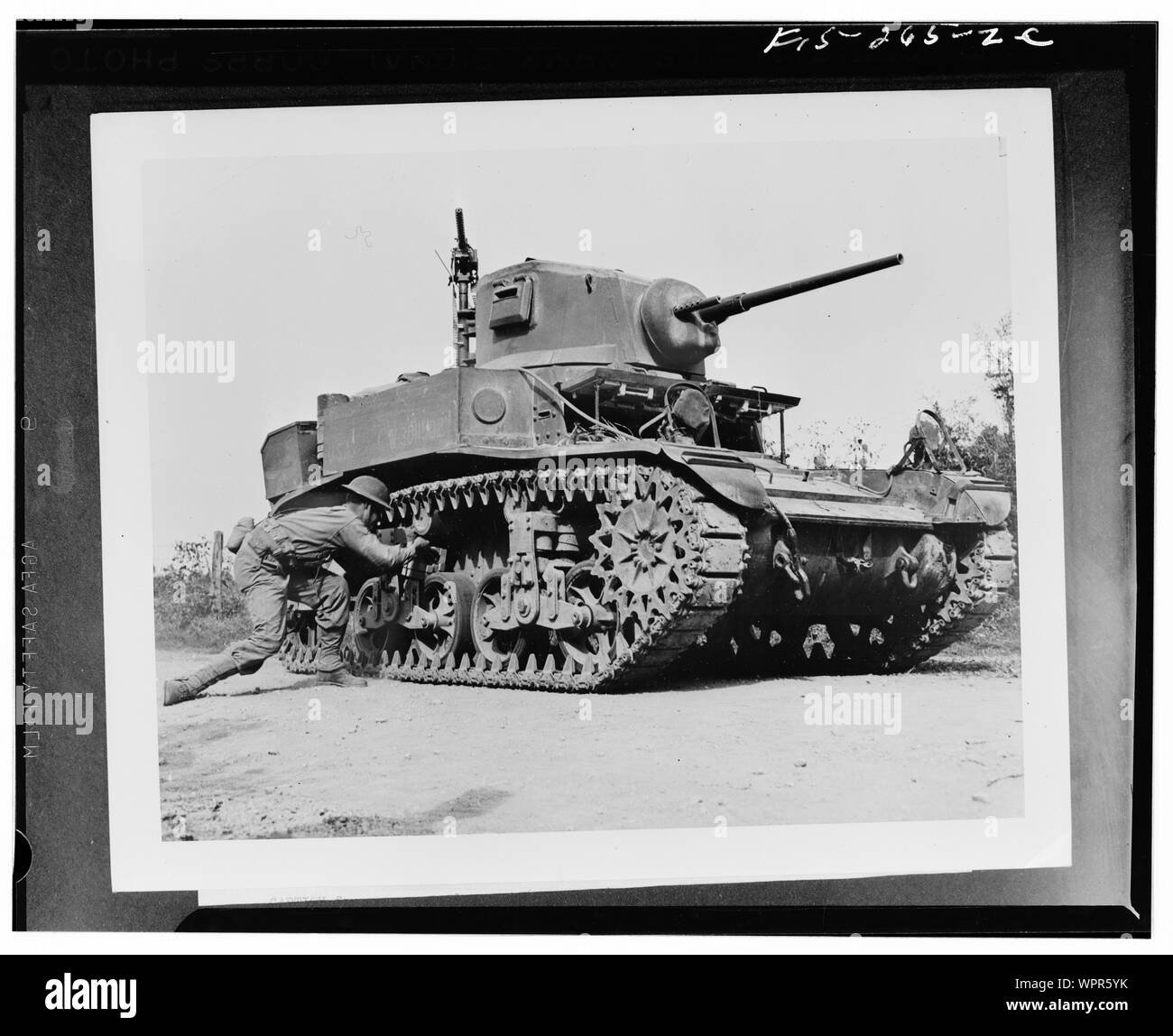 Sergeant Carl Hardy, twenty, of Shelby, North Carolina, stalking an M3A1 Stuart tank on maneuvers with the Second Army in middle Tennessee. The simulated twenty-nine pound TNT satchel charge laid on the bogey of the light tank will wreck it, and possibly kill the four operators within.; Stock Photo