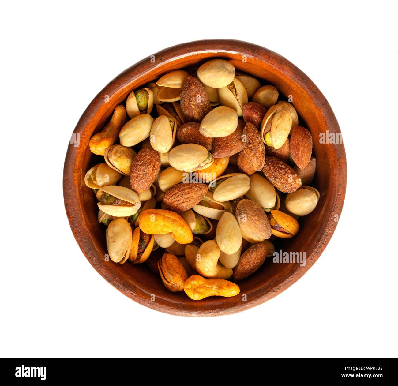 Mixed nuts in a brown ceramic bowl isolated on white background. Healthy snack and food. Salted and spicy pistachios, cashew and almond. Top view. Stock Photo