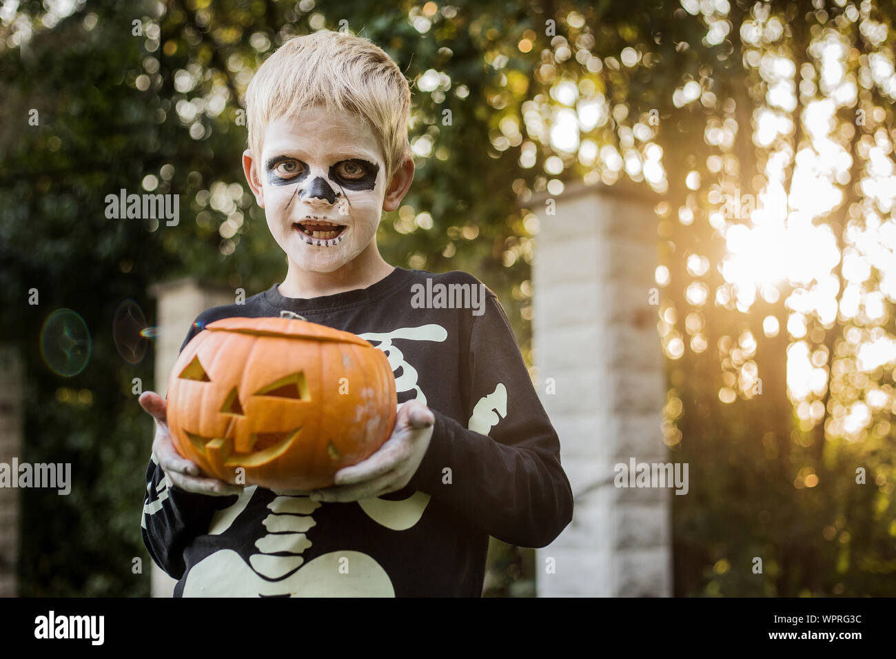 Happy young blond hair boy with skeleton costume holding jack o lantern ...