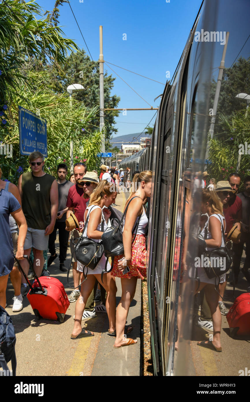 POMPEII, NEAR NAPLES, ITALY - AUGUST 2019: People catching a train at Pompeii Scavi station while others are walking along the platform to the exit Stock Photo