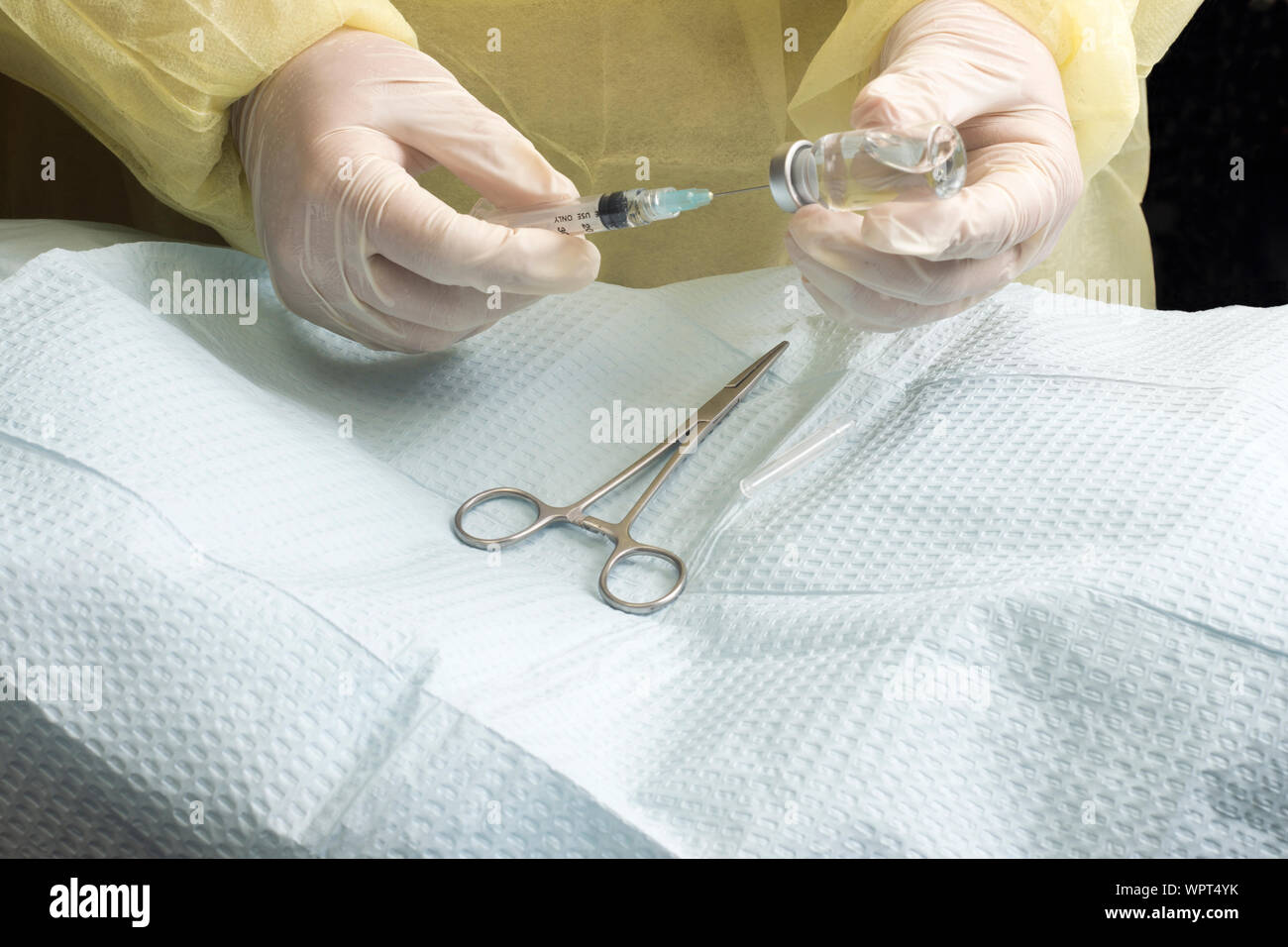 Surgeon draws anestetic into syringe with hemostats on sterile drape below. Stock Photo