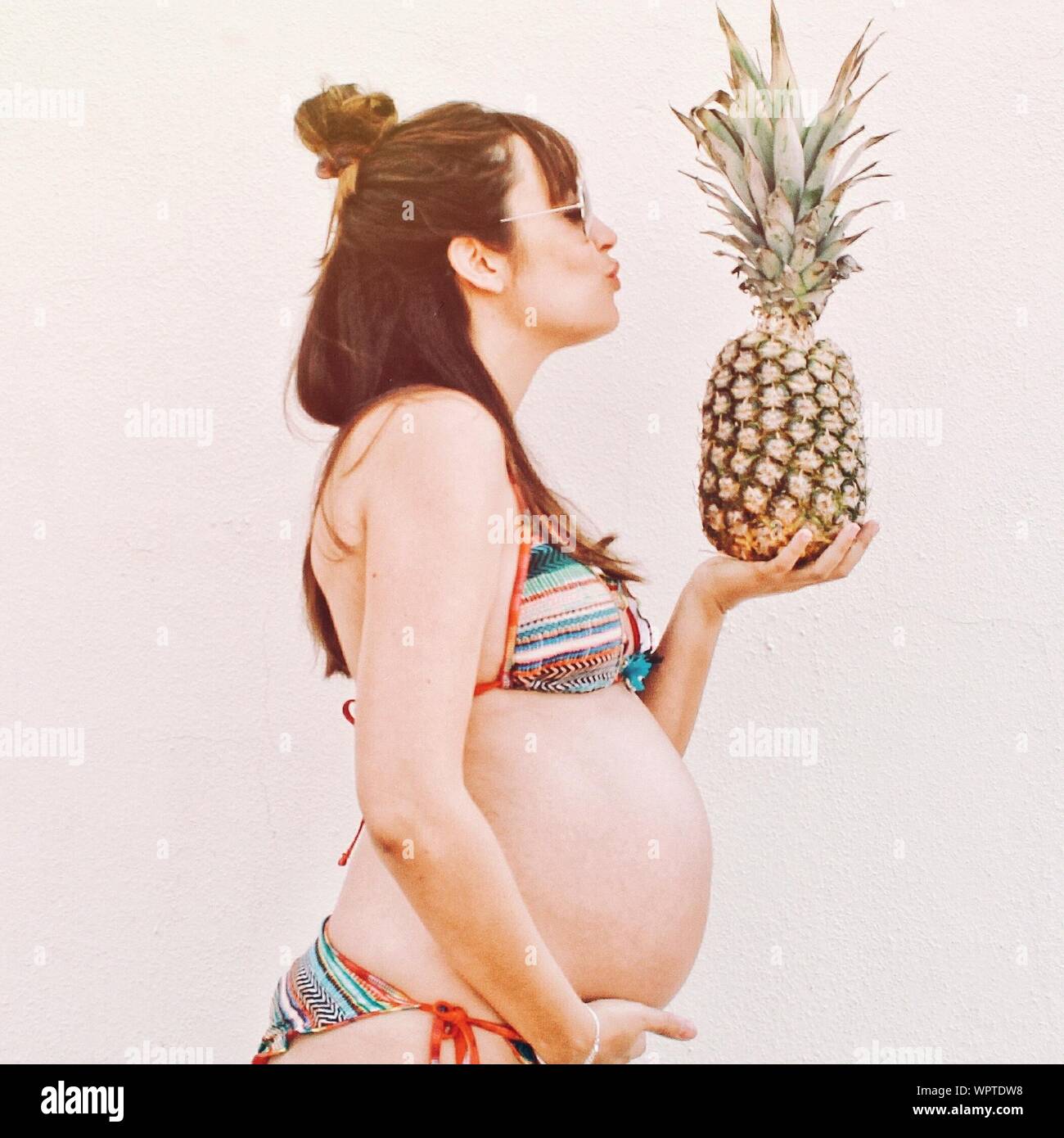 Side View Of Pregnant Woman Holding Pineapple Against White Background