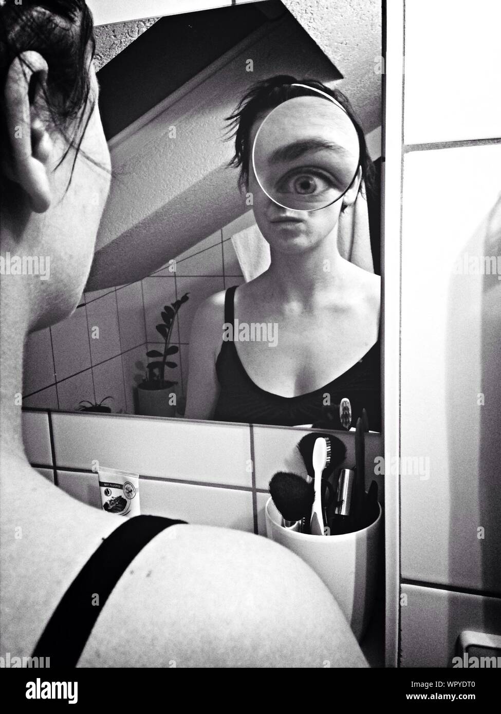 Reflection Of Young Woman In Mirror With Magnified Eye Stock Photo