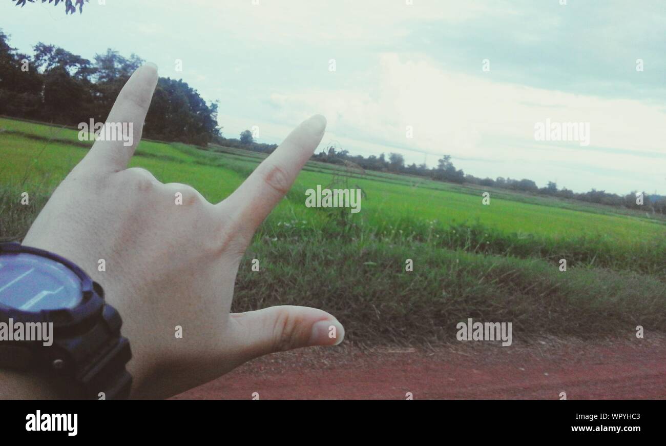 Close-up Of Man Gesturing Shaka Sign On Field Against Sky Stock Photo