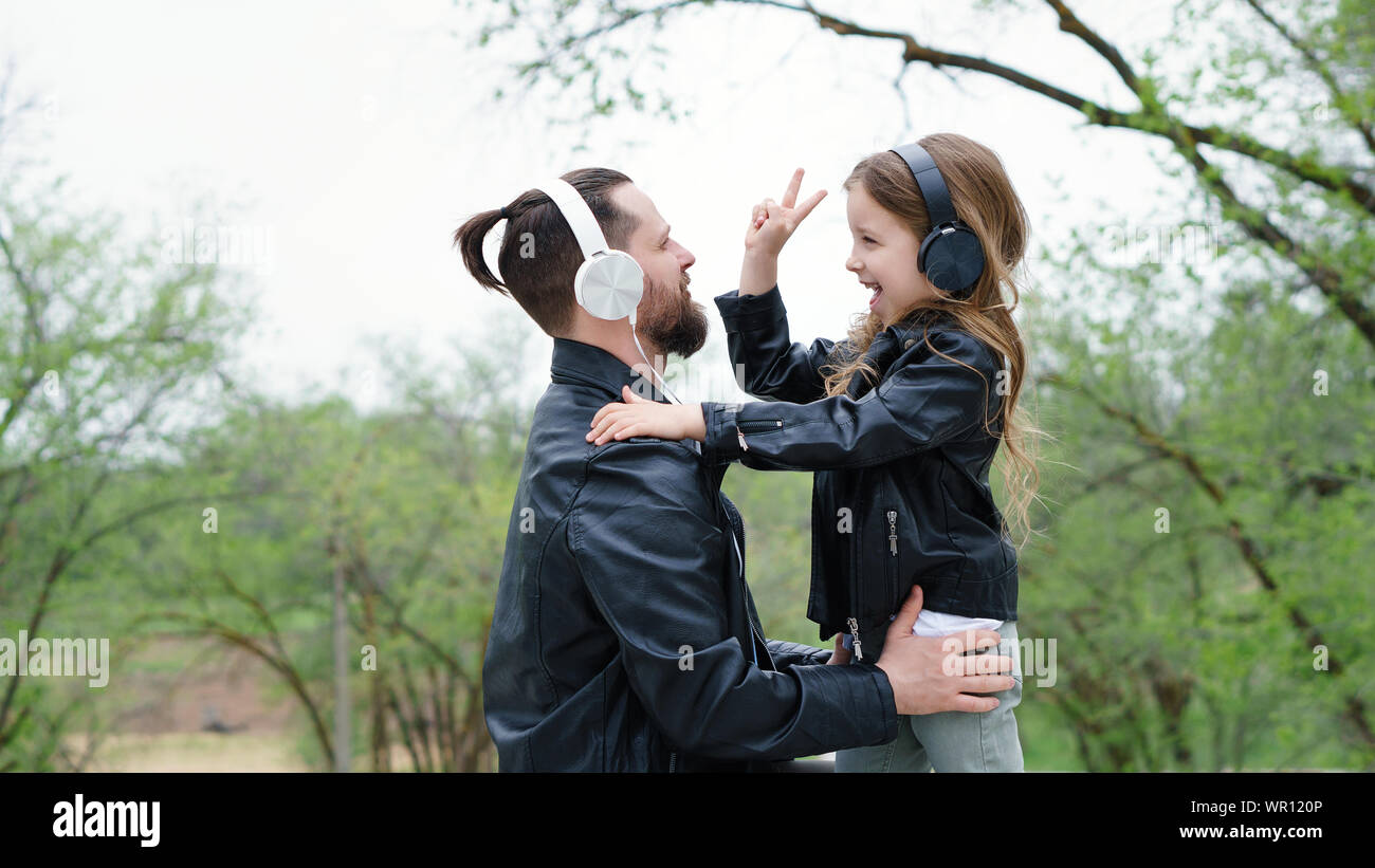 Charming little girl and her handsome young dad in headphones are listening to music. Photo v-sign positive. Family weekend. Time together. Urban casu Stock Photo