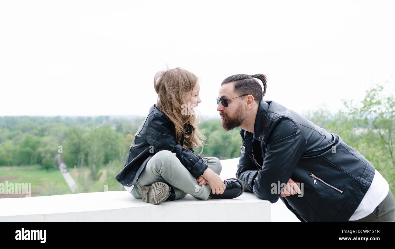 Fashionable stylish family for a walk. Charming schoolchild and her handsome young dad spend time together in the open air. Confidential conversation. Stock Photo