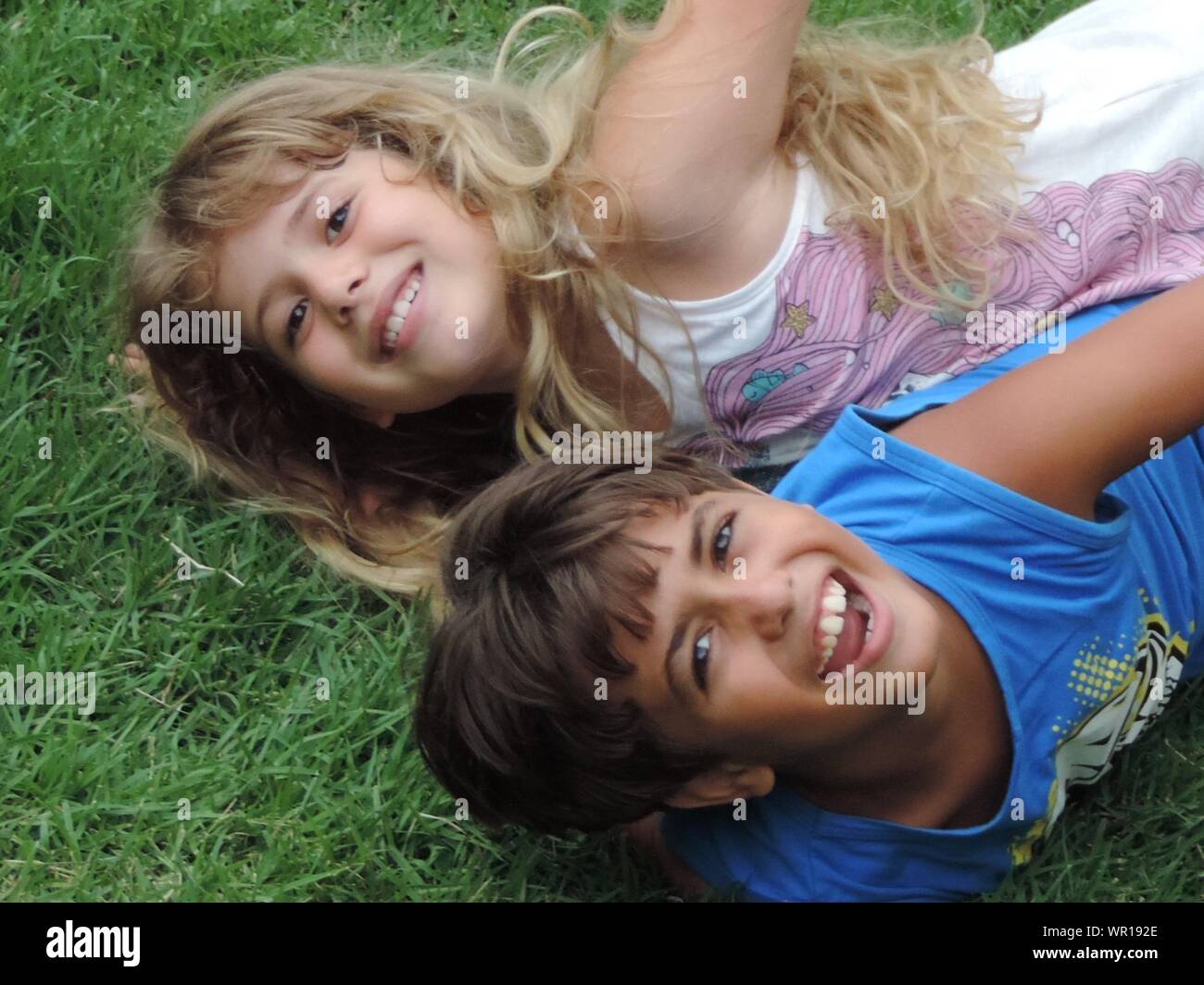 Portrait Of Happy Children Lying On Grassy Field Stock Photo