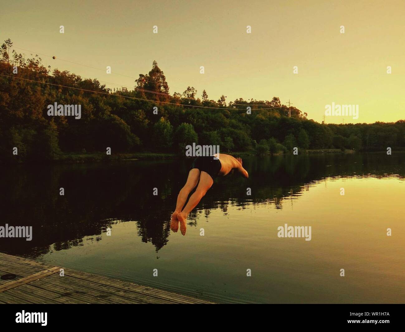 Man Diving Into Lake Against Clear Sky During Sunset Stock Photo