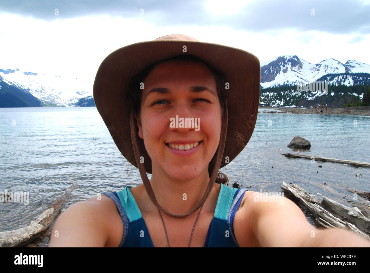 Authentic happy young natural Caucasian woman with a hat adventuring at Garibaldi Lake, taking a selfie in the Canadian glacier landscape Stock Photo