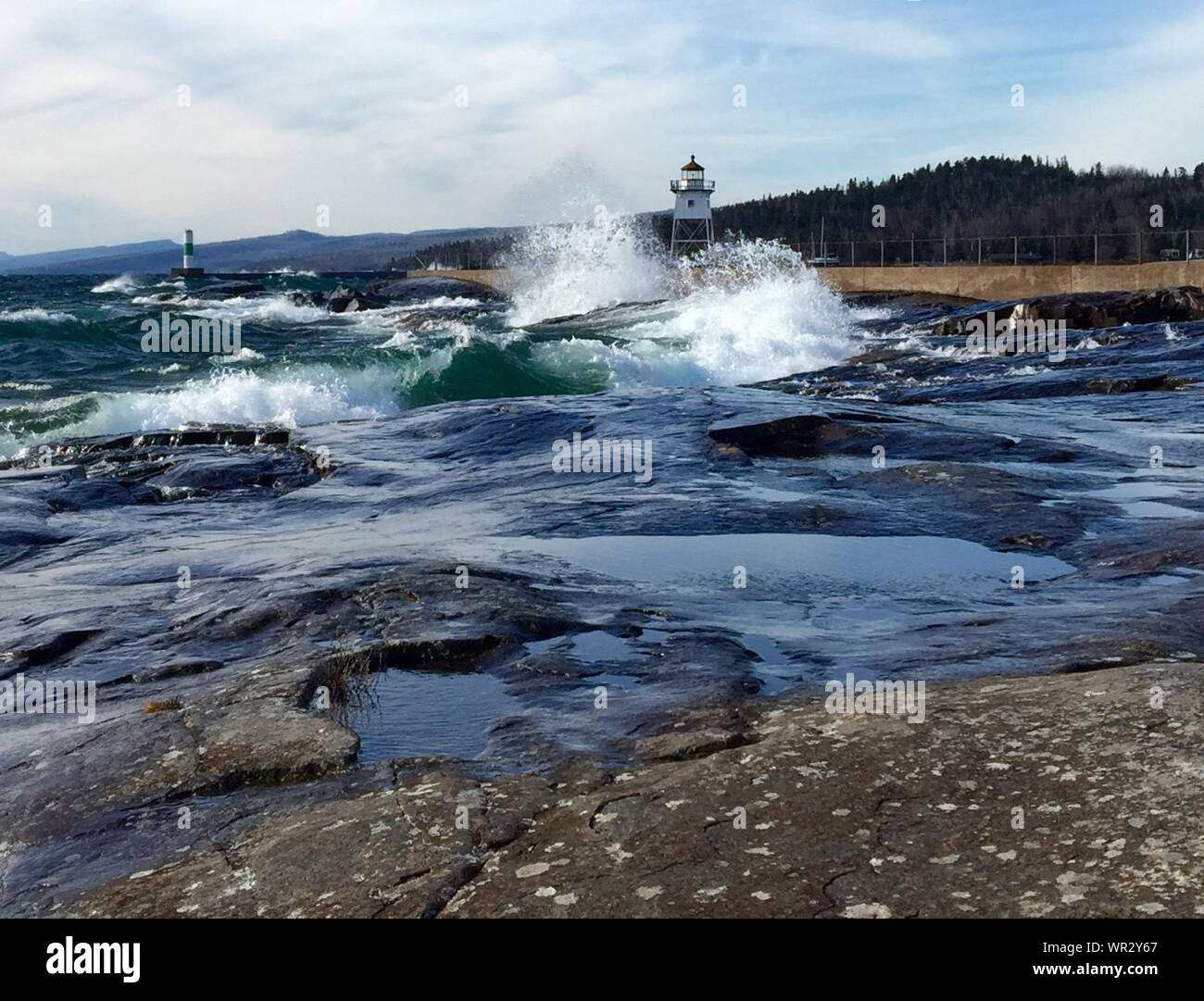 Sea Waves Splashing By Lighthouse Against Sky Stock Photo