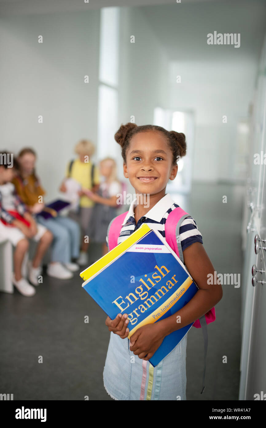 Cute dark-skinned girl holding books while standing at school Stock ...