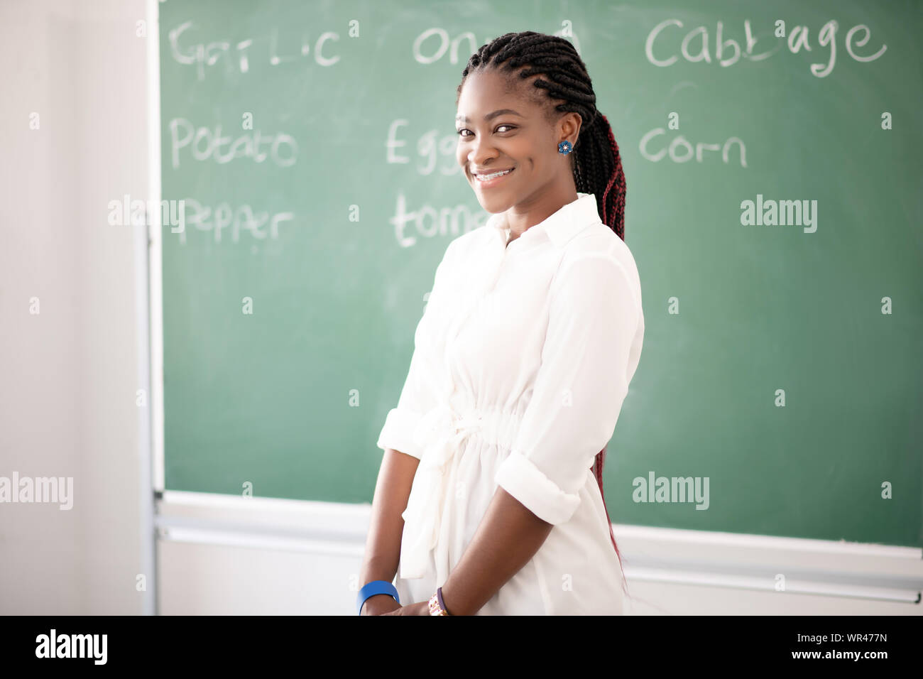 AfricanAmerican teacher smiling while standing near blackboard Stock
