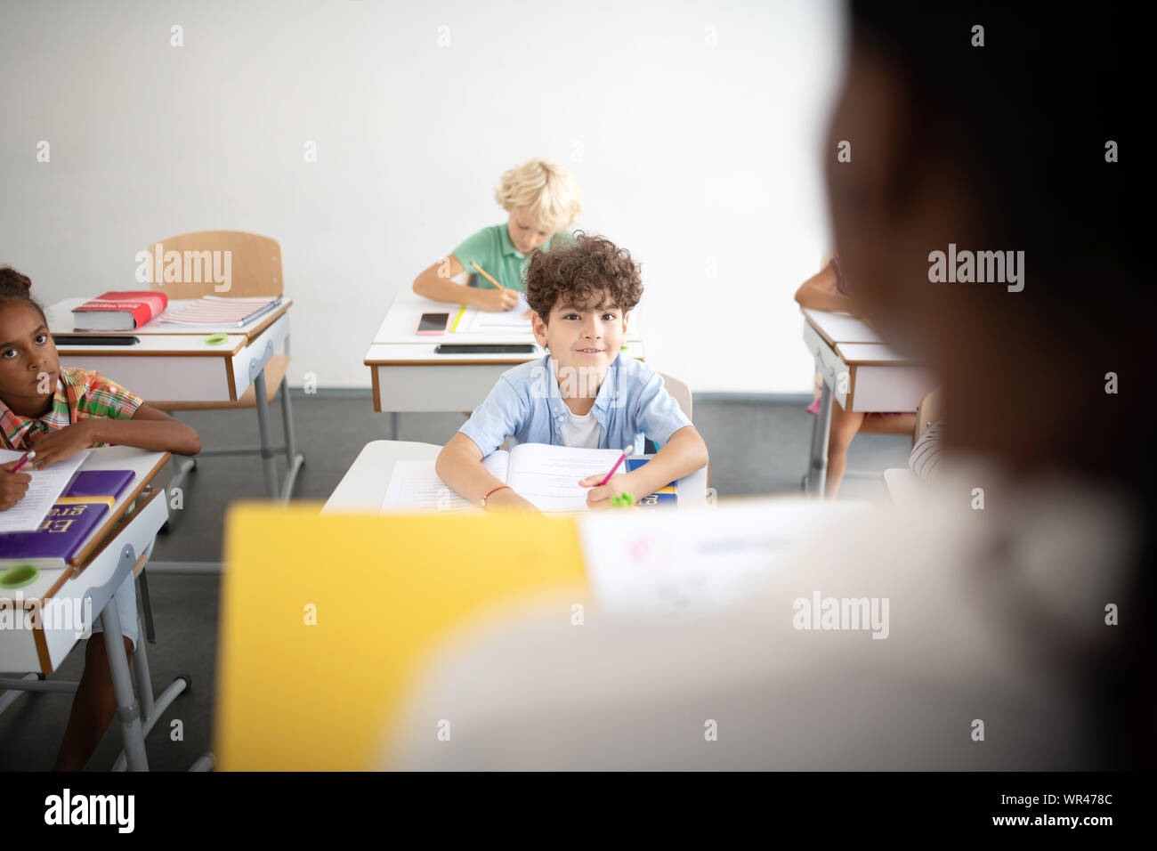 Curly dark-haired boy looking at teacher during the lesson Stock Photo