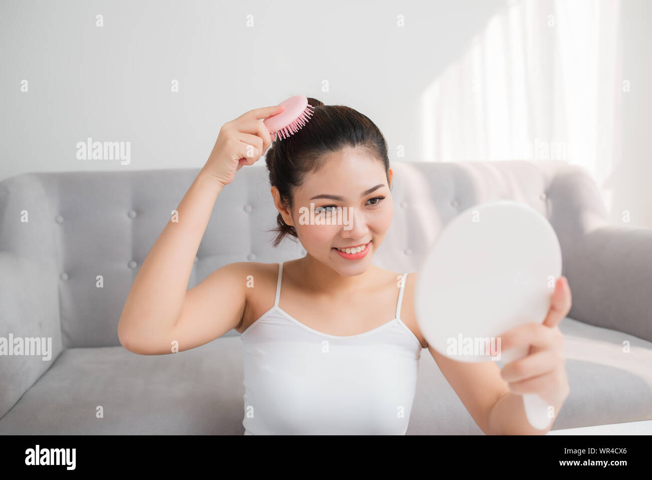 Portrait of beautiful young woman combing her hair, looking mirror Stock Photo