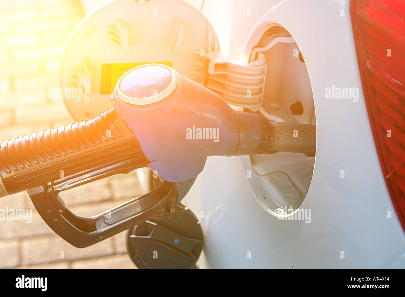 A gun for filling gasoline is inserted into the gas tank of the car. Holding fuel nozzle to refuel gasoline for car. Toned Stock Photo