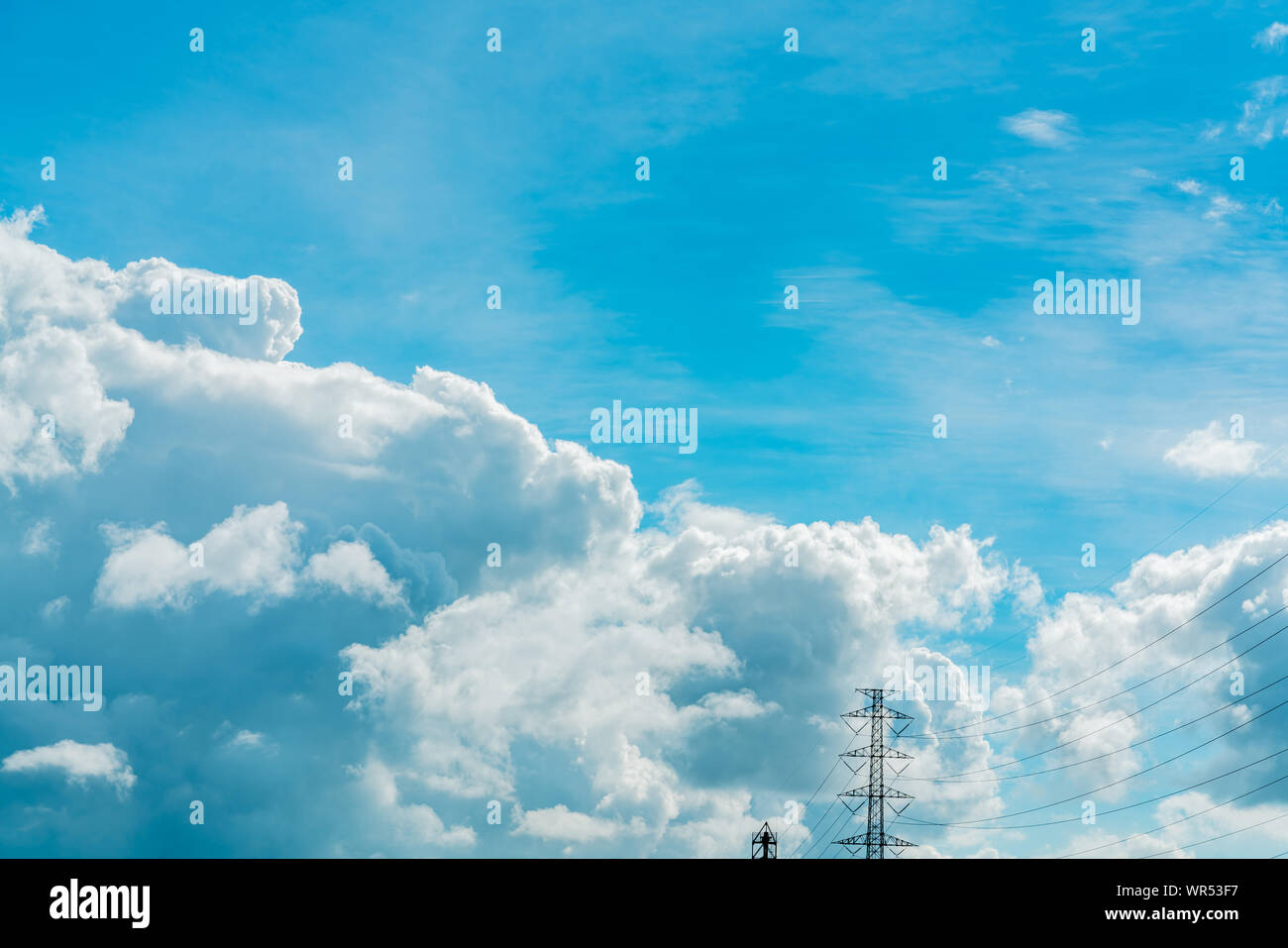 Beautiful blue sky and white cumulus clouds above transmission lines and high voltage electric tower. Cloudscape background. Blue sky and fluffy white Stock Photo