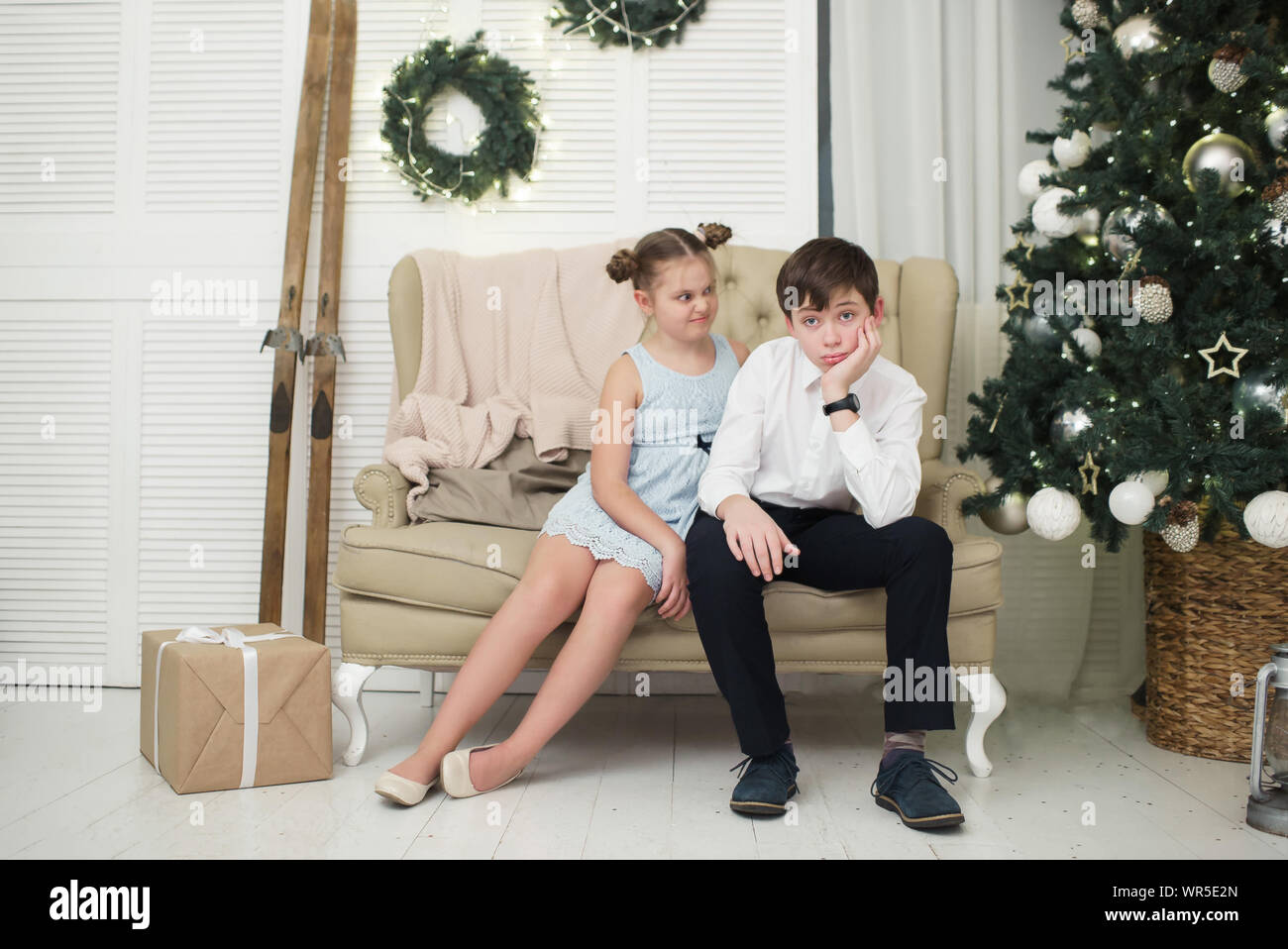 The sad brother and the evil sister are sitting by the Christmas tree Stock Photo