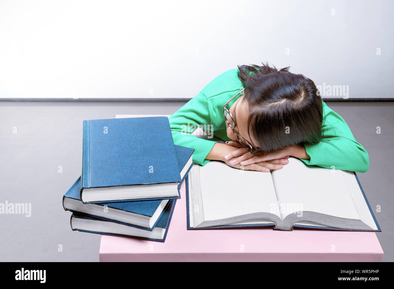 Asian cute girl with glasses fall asleep on a book on the desk at home Stock Photo