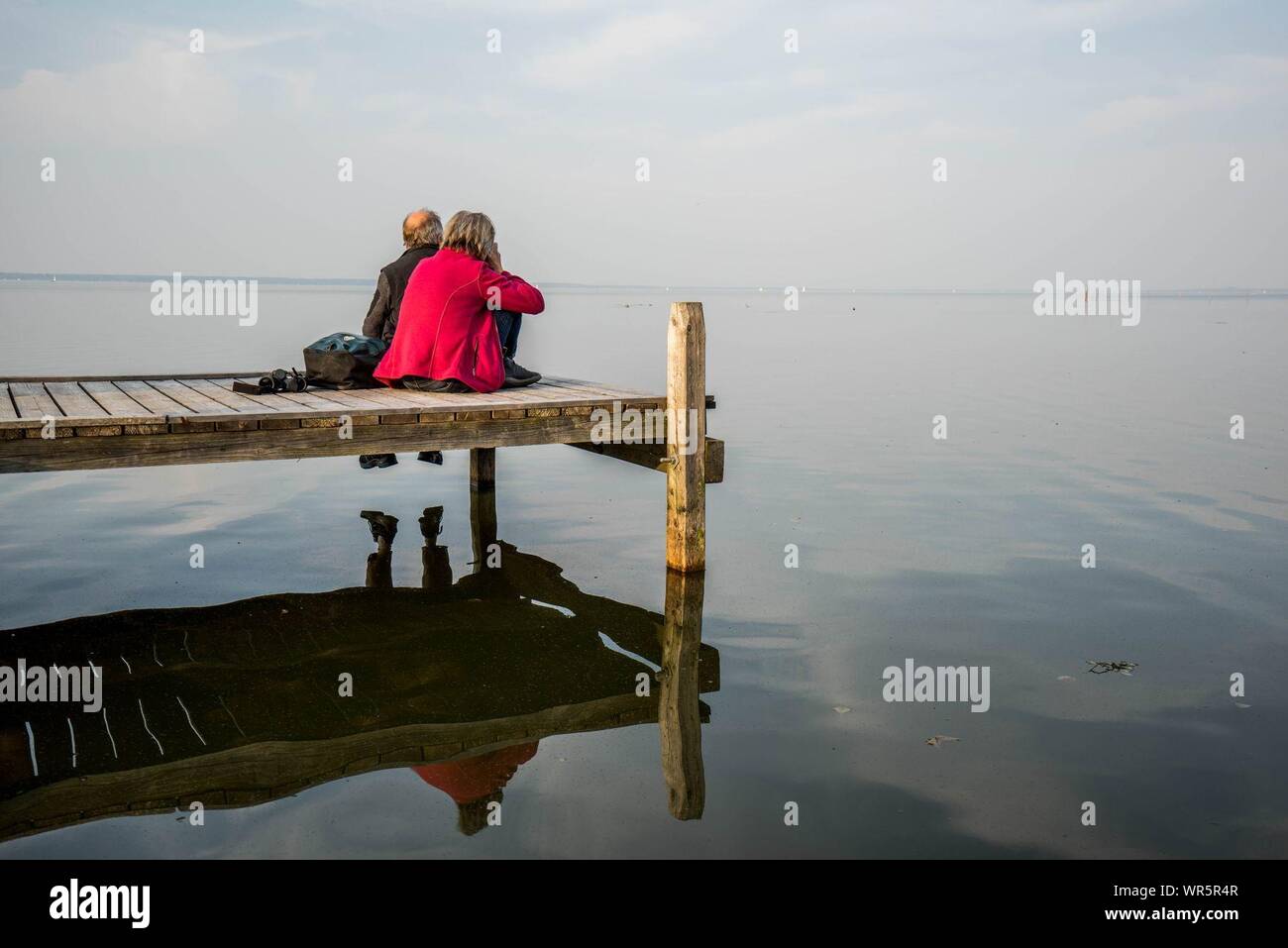 Men Relaxing On Jetty At Lake Steinhude Meer Against Sky Stock Photo