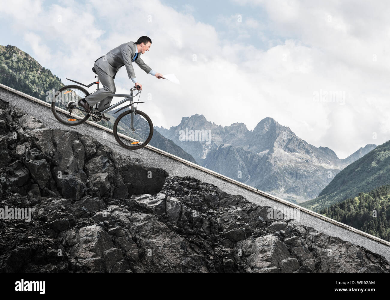 Businessman with paper documents in hand going downhill on bike
