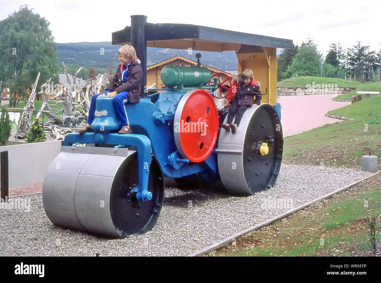 Historical archival 1970s family touring holiday colourful steam roller in children playground two boys & Mum with girl at back how we were in 70s Aviemore Scottish Highlands UK Stock Photo