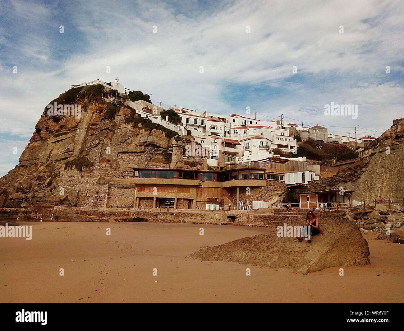 Woman Sitting On Rock Against Buildings At Azenhas Do Mar Stock Photo